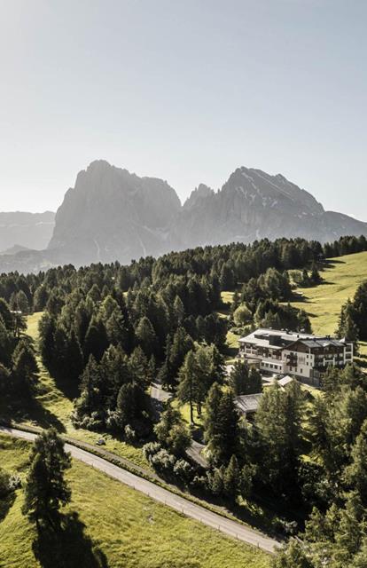 Blick auf unser Hotel inmitten grüner Almwiesen und Wälder, mit den Dolomiten majestätisch im Hintergrund.