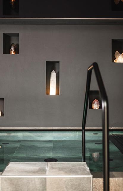 Modern indoor pool with clean lines, surrounded by dark walls featuring illuminated crystals set into niches.