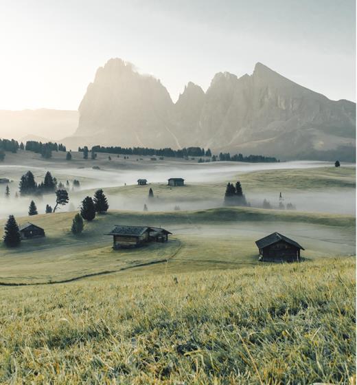 Mystical morning on the Alpe di Siusi – fog blankets meadows and huts beneath dramatic peaks