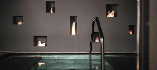 Modern indoor pool with clean lines, surrounded by dark walls featuring illuminated crystals set into niches.