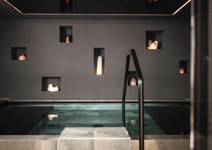 Piscina coperta moderna dalle linee pulite, circondata da pareti scure con cristalli illuminati incastonati in nicchie.