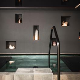 Modern indoor pool with clean lines, surrounded by dark walls featuring illuminated crystals set into niches.