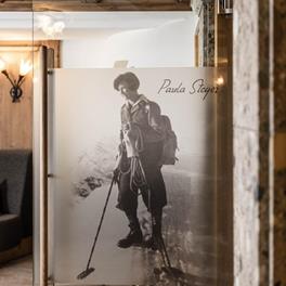 Fotografie einer historischen Aufnahme von Paula Steger beim Skitourengehen, abgebildet auf einer Glaswand in einem gemütlichen Innenraum mit Holz- und Steinelementen.