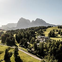 Blick auf unser Hotel inmitten grüner Almwiesen und Wälder, mit den Dolomiten majestätisch im Hintergrund.