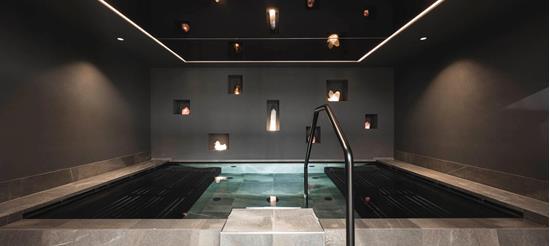 Modern indoor pool with clean lines, surrounded by dark walls featuring illuminated crystals set into niches.