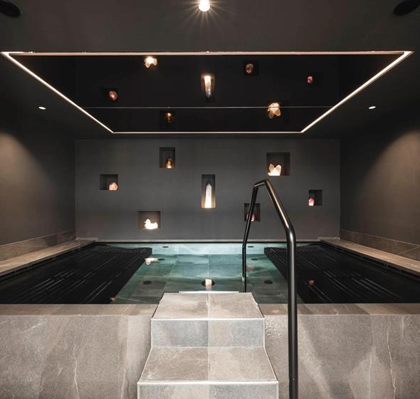 Modern indoor pool with clean lines, surrounded by dark walls featuring illuminated crystals set into niches.