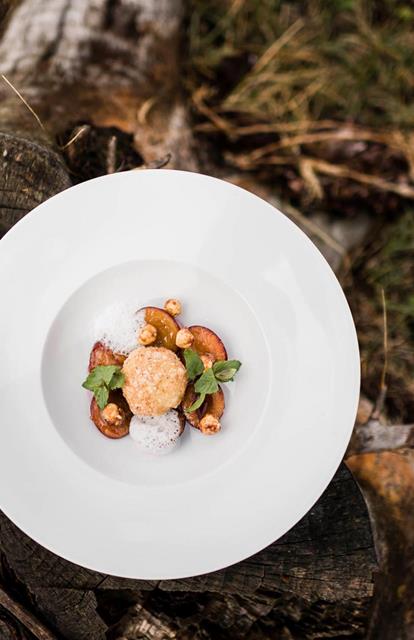Dessert with nuts, foam, plums and mint on a tree stump outdoors, with cutlery and napkin