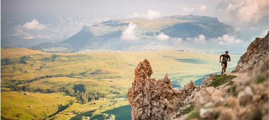Trail runner on a mountain ridge with wide view of green pastures and hills in the background.