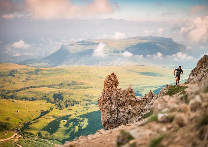 Trail runner on a mountain ridge with wide view of green pastures and hills in the background.