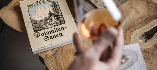 A person is holding a glass with an amber-coloured drink and is looking at a book titled Dolomite Legends