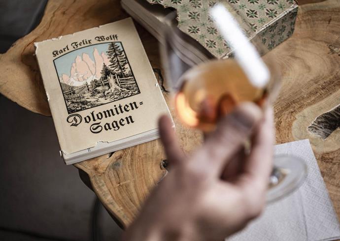 A person is holding a glass with an amber-coloured drink and is looking at a book titled Dolomite Legends