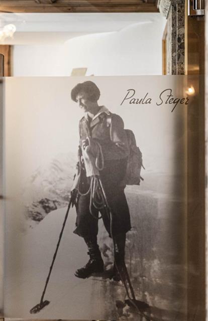 Fotografie einer historischen Aufnahme von Paula Steger beim Skitourengehen, abgebildet auf einer Glaswand in einem gemütlichen Innenraum mit Holz- und Steinelementen.