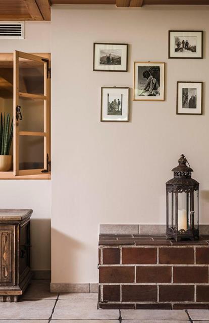 Traditionally furnished room with green tiled stove, antique wooden chest, open interior window with a plant, and historical black-and-white photographs on the wall.