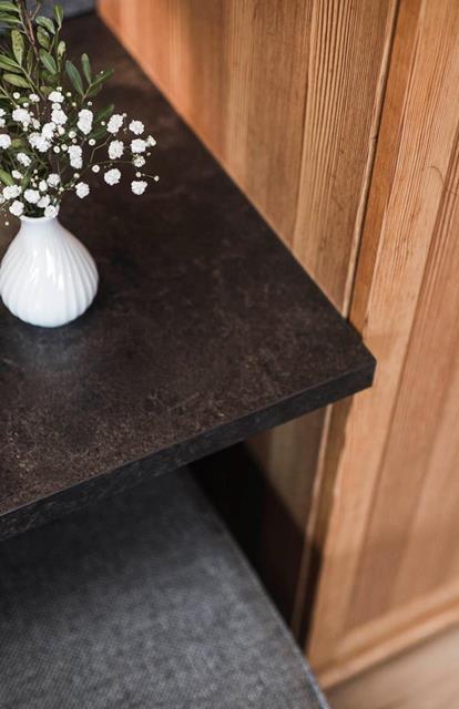 Weiße Keramikvase mit zarten weißen Blüten und grünen Zweigen auf einer dunklen Tischplatte