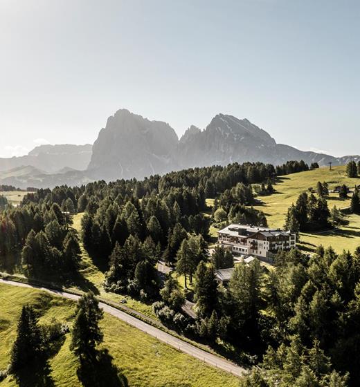 Blick auf unser Hotel inmitten grüner Almwiesen und Wälder, mit den Dolomiten majestätisch im Hintergrund.